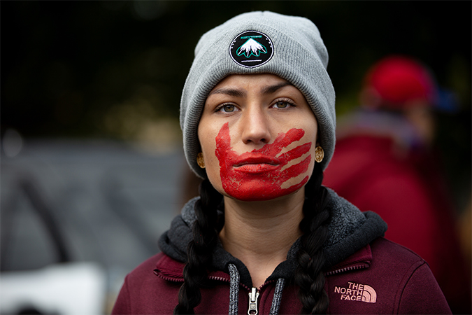 Young Native American woman with a red paint handprint over her mouth.