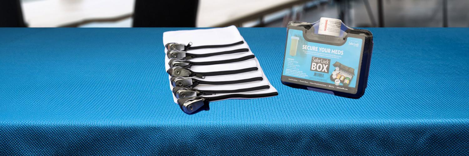 BH: Lock up your meds Table with bright blue tablecloth. Locking bag and locking box are on top of the table.