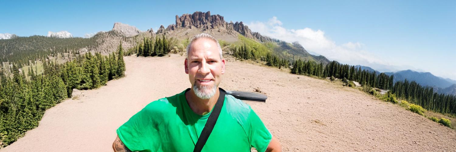 Voices of ERB: Tim Hein Tim Hein hiking with a mountain behind him.