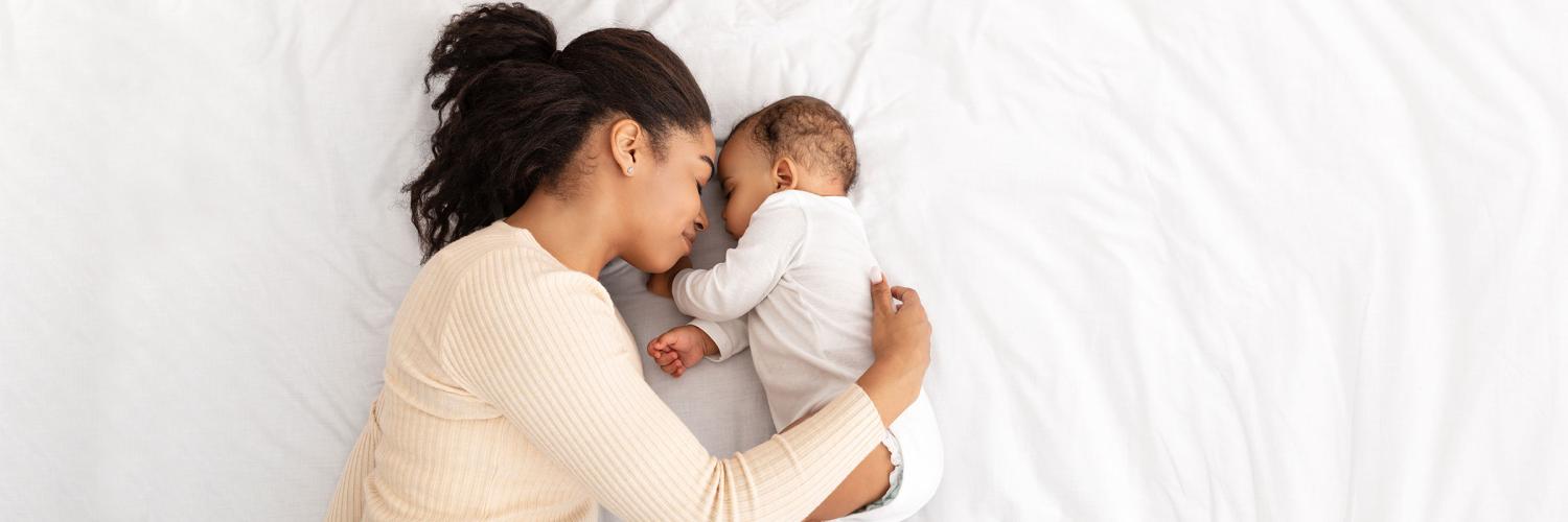 HE Spotlight: Black infant health care Young black mother cuddles her infant on a bed of white sheets.