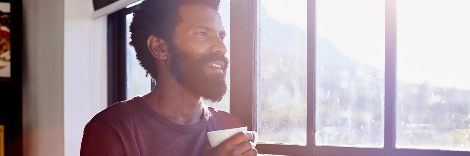 Voices of ERB: Hidden diagnosis, high blood pressure Young man drinking coffee, looking thoughtfully out a window