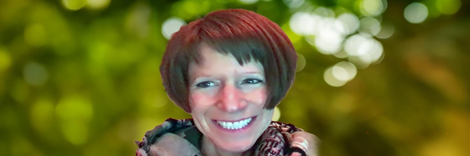 A photo of a female individual smiling with a blurred nature background scene.