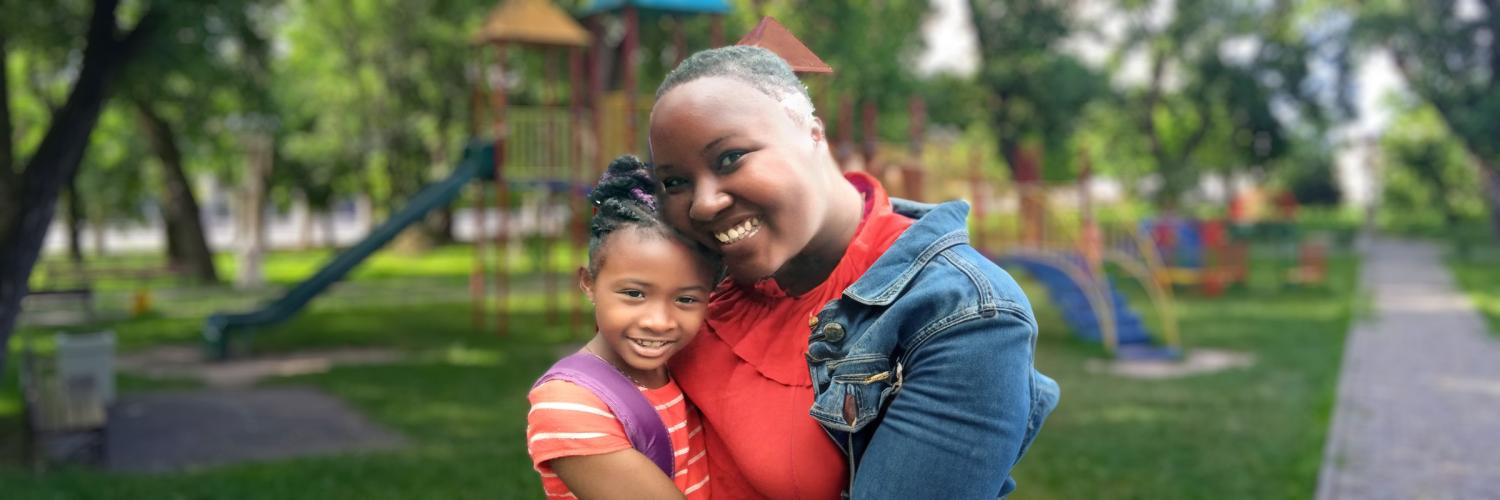 Outdoor photo of mother and young daughter at a park.