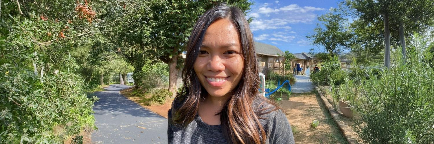 Photo of a female smiling while standing in a hiking trail on a sunny day.