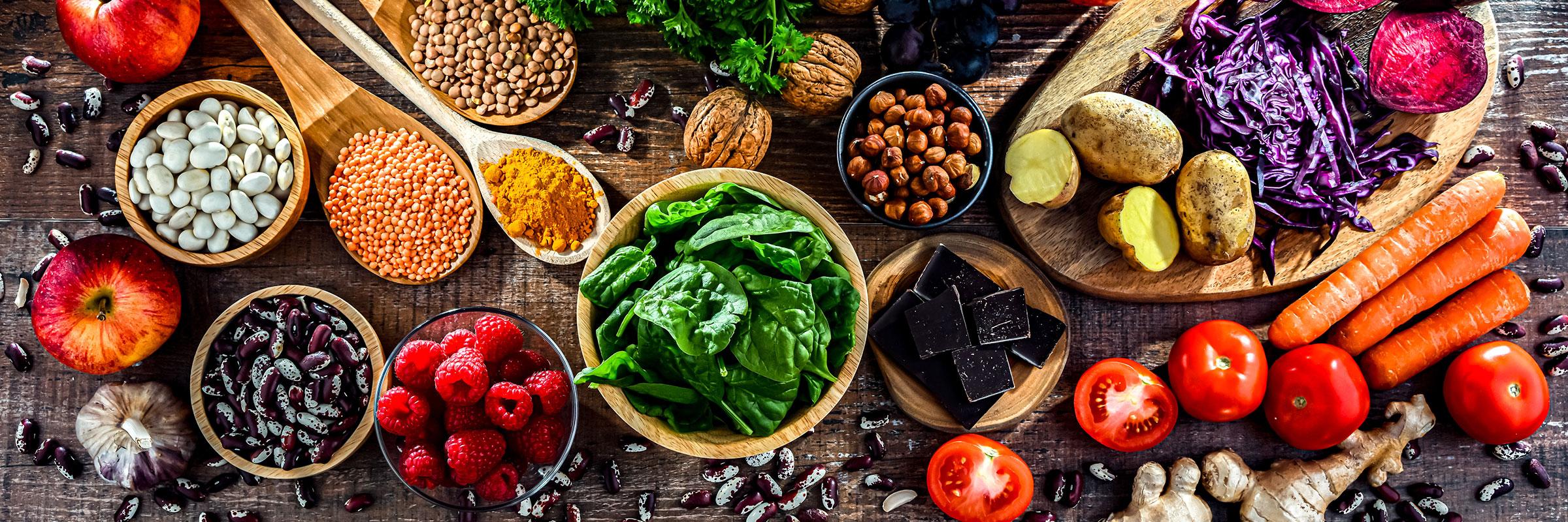 A table full of healthy foods including spinach, legumes, tomatoes.