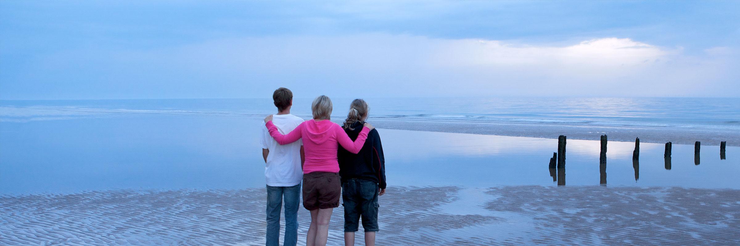 Woman with young man and young woman standing on the beach looking out at the water.