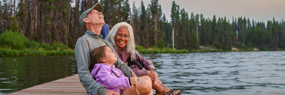 Two gray-haired adults and a child enjoy sitting by the lakeside