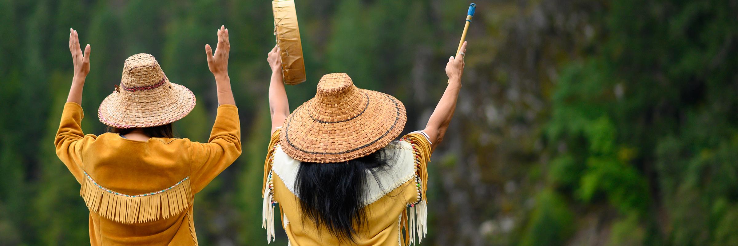 Two Pacific Northwest Native American women dancing with their hands raised to the mountains.