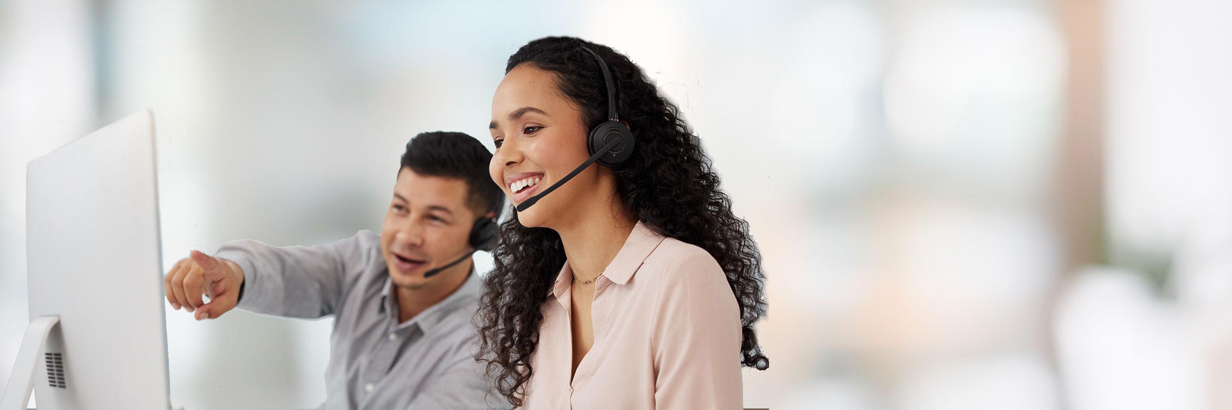 Latin man and woman with headsets in front of computer. The man is pointing at the computer.