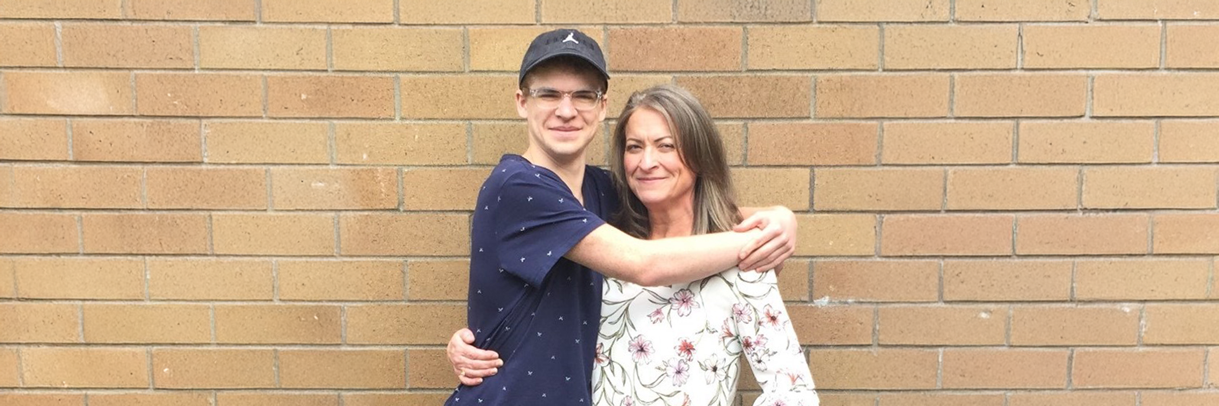 Photo of a mother and son hugging each other in front a brick wall