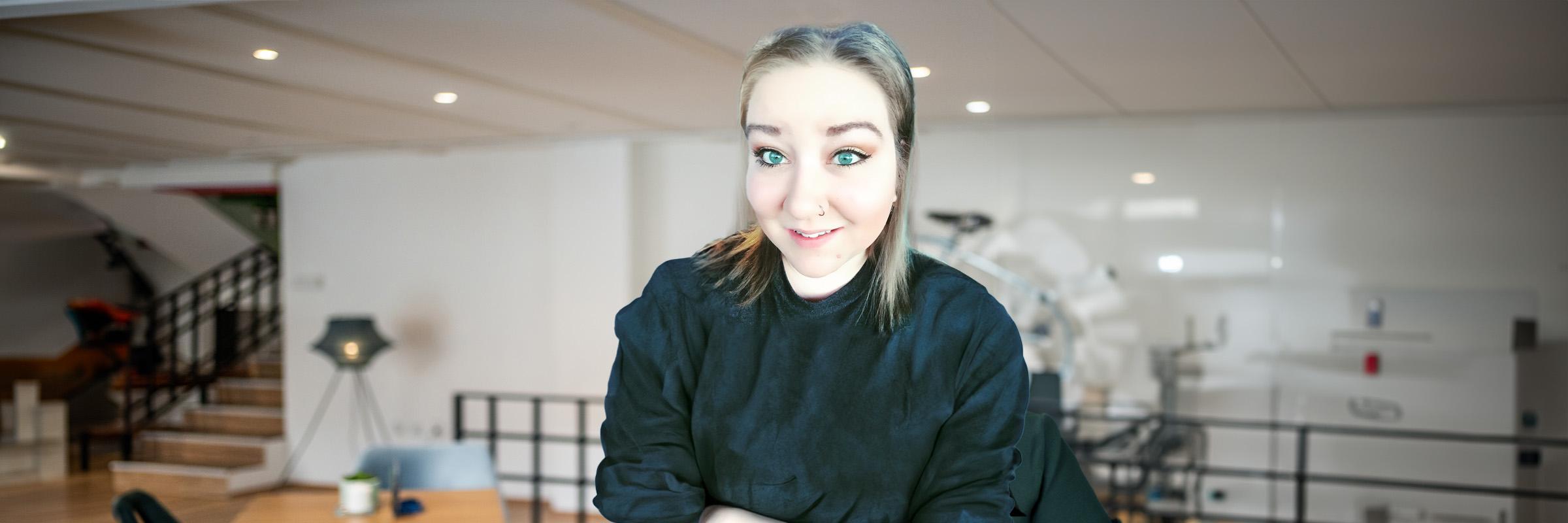 A photo of a smiling female in a black sweater with a studio apartment background. 