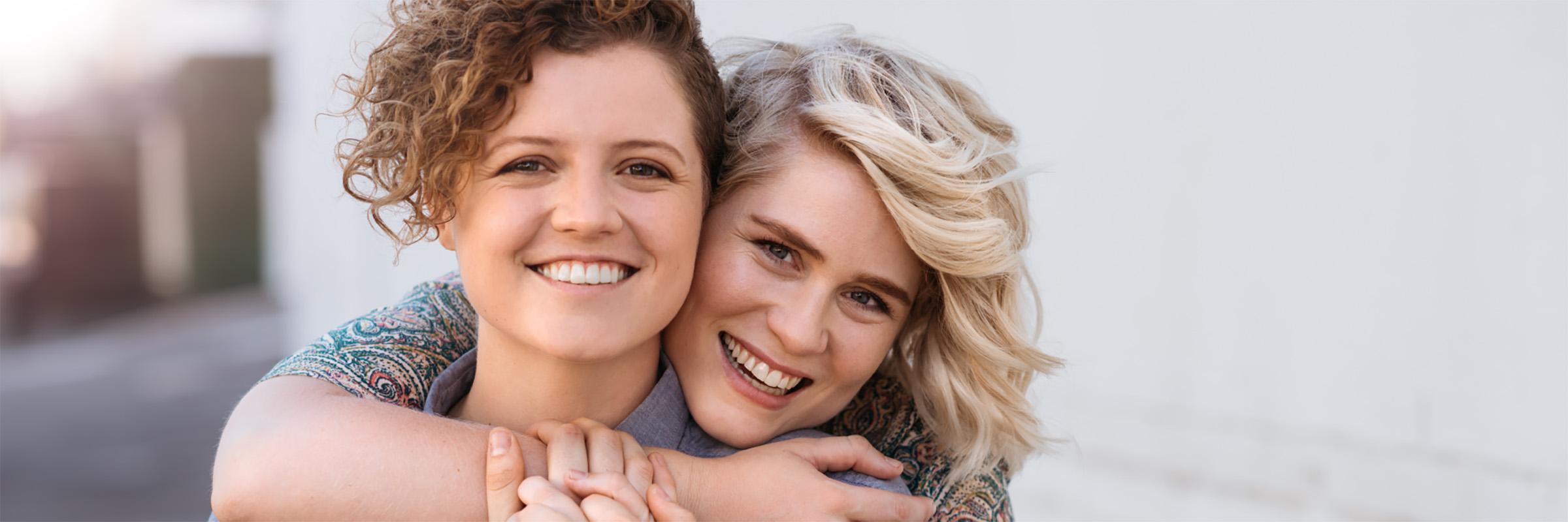 A photo of two female individuals hugging and smiling. 