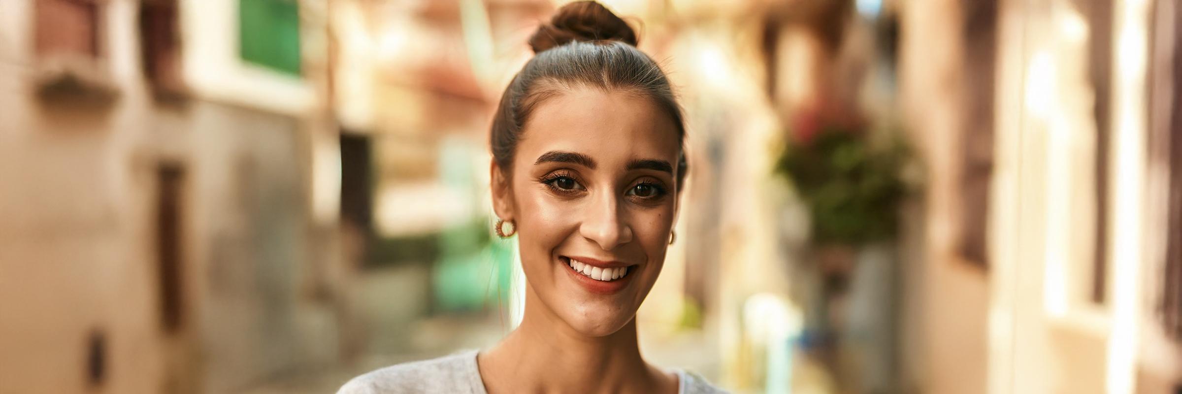 A headshot photo of a female presenting individual smiling with a blurred background of a city. 