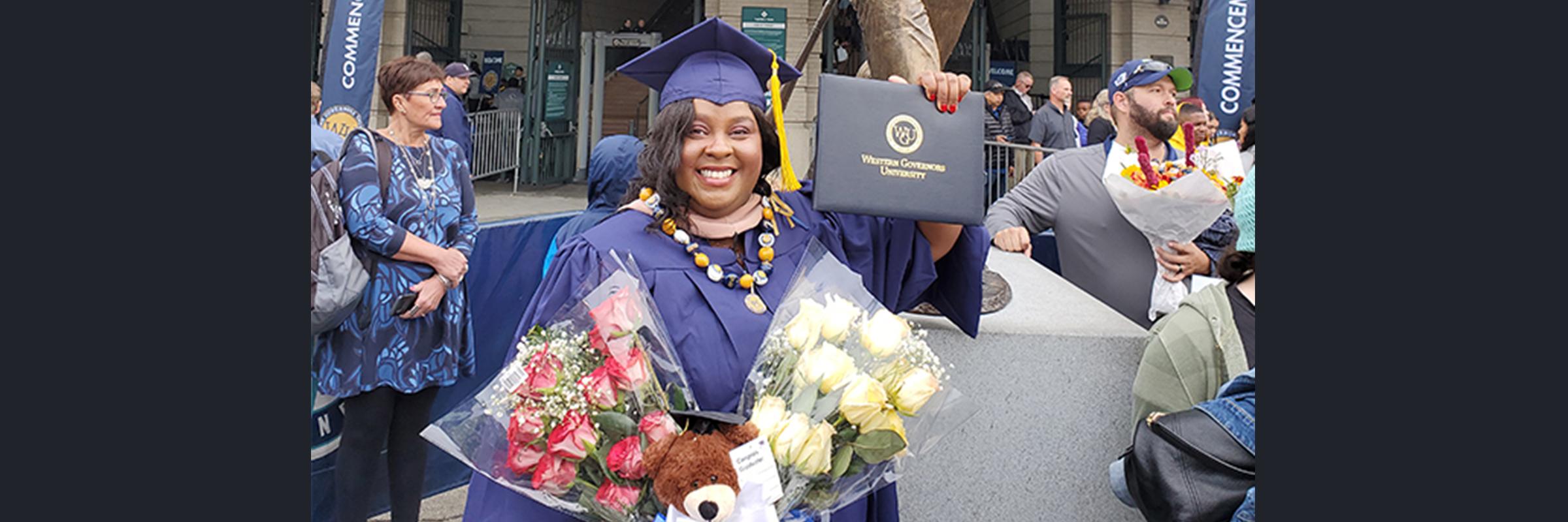 Erika Campbell stands in front the university in purple robes, displaying her master's degree