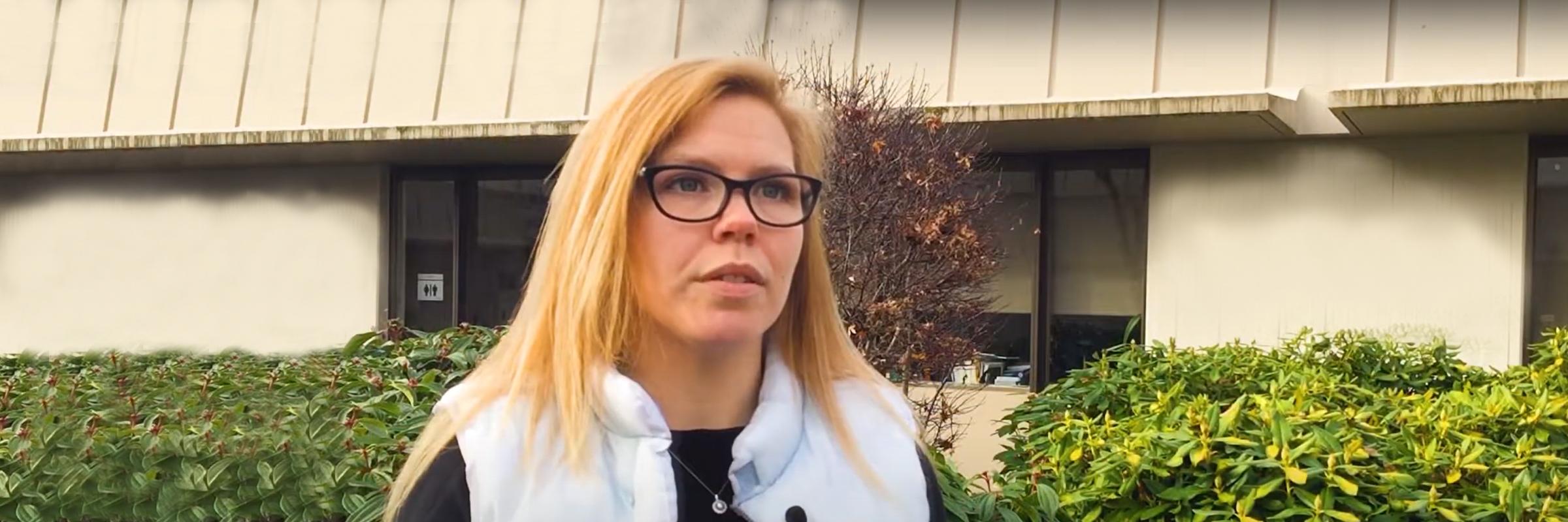 Julie Liles in front of a health clinic wearing a white vest and black shirt.